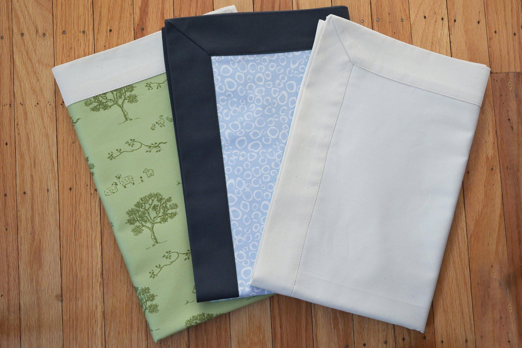 dog bed coverlet fabric samples in green tree pattern, blue with navy trim, and white